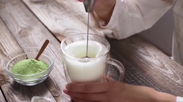 Soy Milk In Transparent Glass Cup Is Whipped On Wooden Kitchen Table. Preparation Of Matcha Tea alt