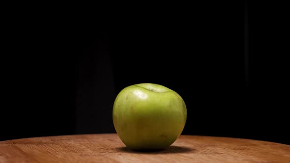 A green apple on a wooden board on a black background. The camera flies around alt