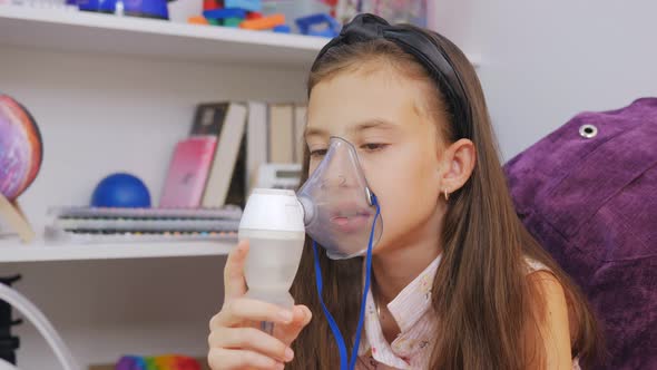 Little Girl Makes Inhalation with Medical Nebulizer While Sitting at the Table alt