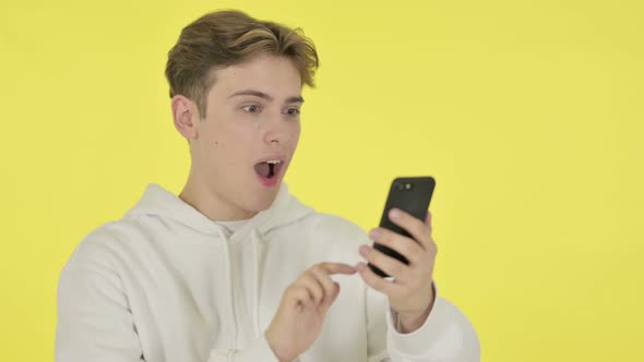 Young Man Celebrating on Smartphone on Yellow Background alt