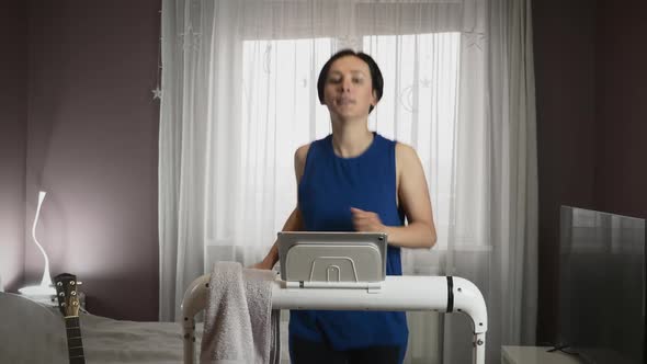 Fit athletic female is running on treadmill at home alt