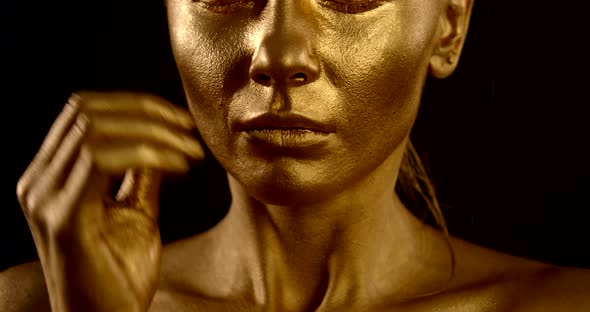 Close-up of a Woman's Face with Golden Glowing Skin and Closed Eyes on a Black Background. the Girl alt