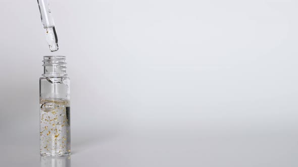 Serum with Gold Drops Falling From the Cosmetic Pipette on White Background alt