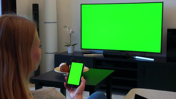 Woman Sits on Couch in Living Room and Works on Green Screen Phone and Watches TV alt