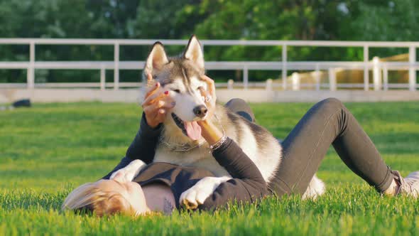 Beautiful Young Woman Playing with Funny Husky Dog Outdoors in Park alt