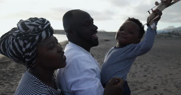 African parents and little son having fun with wood airplane on the beach alt