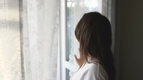 Happy Optimistic Young Woman Opening Curtain Looking Through Window