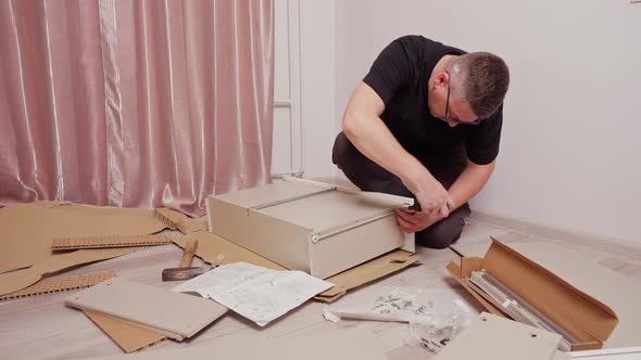 a Young Man on the Floor Collects a Drawer for a Chest of Drawers Next to Boxes and Other Details of alt