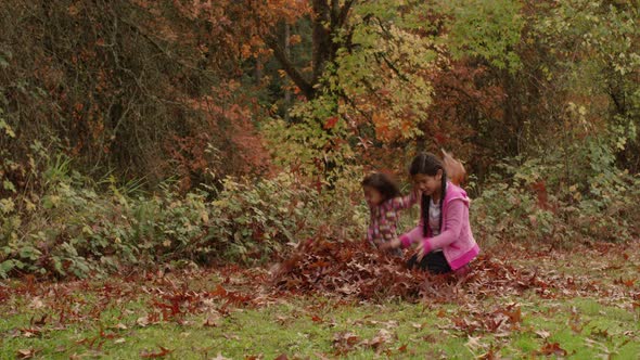 Two young girls in Fall jump into pile of leaves