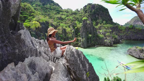 Woman Sitting On Limestone Rocks Taking Photo With Smartphone alt