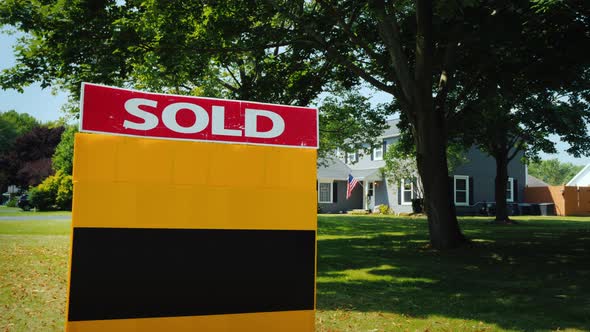 A Plate with the Words Sold, in the Background a Typical American House with the Usa Flag alt