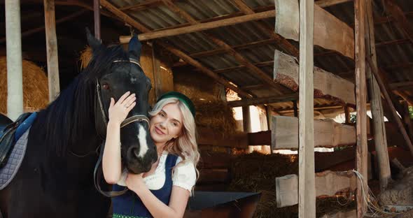 Attractive Girl Caresses the Horse's Black Head and Smiling at a Stable alt