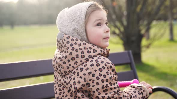 Caucasian Preschool Girl Portrait with Pink Scooter in the Park on Sunny Cold Day in Spring alt