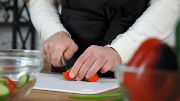 Chef cook man in black apron sliced fresh cherry tomato on board in home kitchen alt