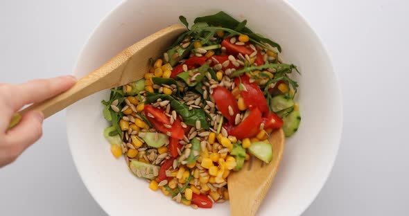 Close up - Woman stirring wooden spoon of fresh appetizing vegan salad in the bowl. Concept of vegan