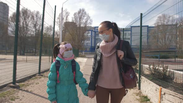 Mom Holds Her Daughter's Hand and Together They Walk Down the Street in Protective Masks