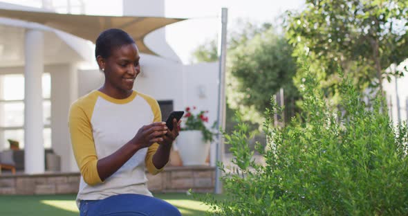 Happy african amercian woman gardening, taking picture of plants in garden alt