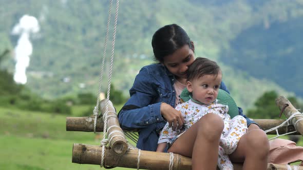 On a Wooden Swing with a Net a Cute Woman with a Small Child Spends Free Leisure Time