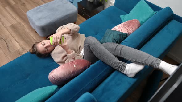 High Angle View Excited Carefree Teenage Girl Lying on Cozy Couch Reading Phone Message in alt