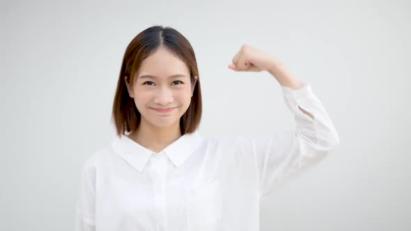 Cheerful Asian girl raising her arms and showing off her muscles looks confident