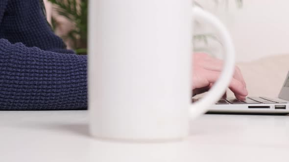 On the Table Is a Cup of Coffee and a Man Working in the Office on a Laptop