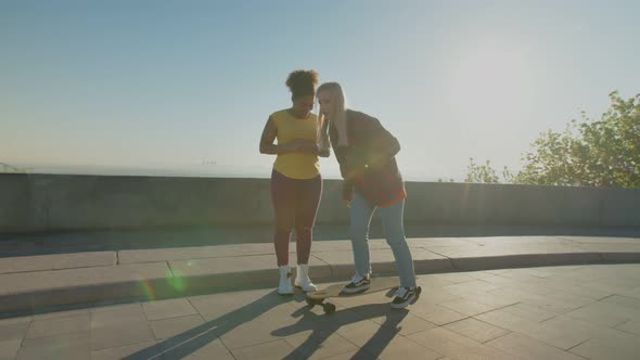 Skillful Woman Teaching Black Female Skateboarding Outdoors at Dawn alt