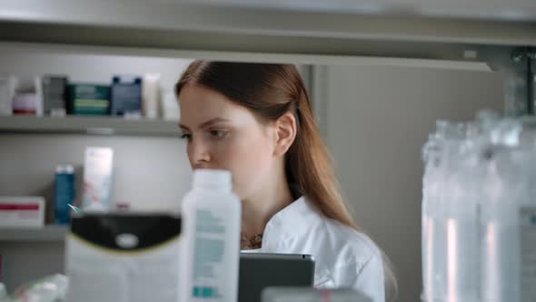 Female Pharmacist Checks Medical Products with a List on a Digital Pad alt