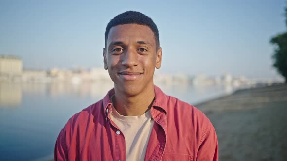 African American Man Stands Smiling Against Blurry Beach alt