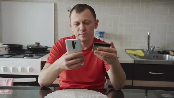 A man sitting in the kitchen pays for an online purchase through a mobile phone alt