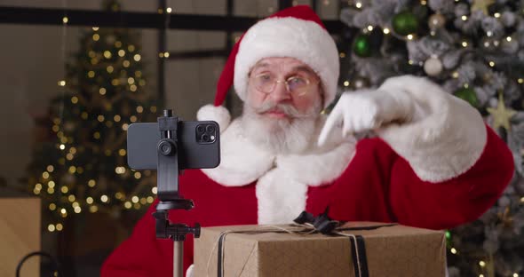 Focus on Smartphone Mounted on Tripod Against the Blurred Background of a Cheerful Santa Claus alt