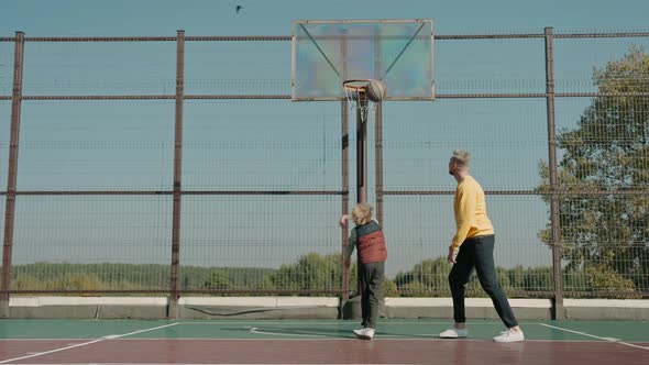 Boy Learns to Throw Basketball Ball with Father on a Court on a Sunny Day