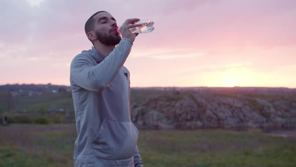 Exhausted Sportsman Drinking Water After Workout in Field