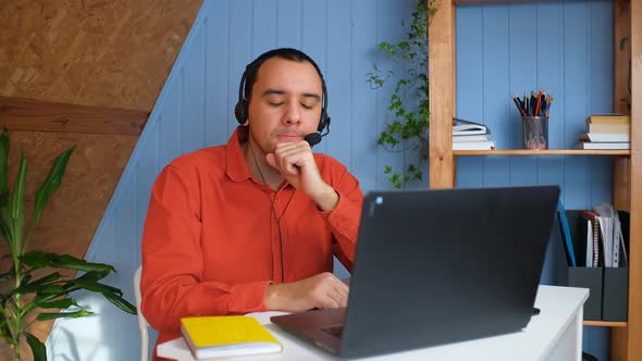 Sad Man in Headphones Sit at Desk in Front of Laptop Thinking alt