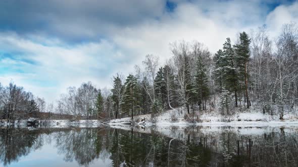 Winter landscape with forest on the lake, clouds in the sky