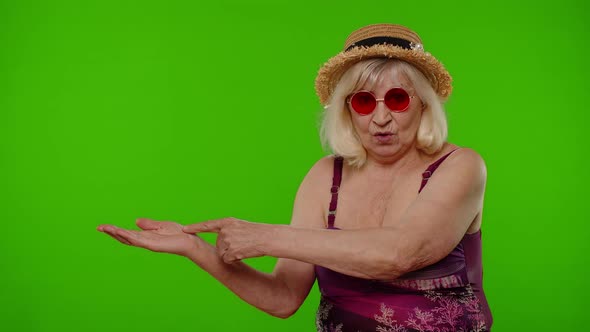 Senior Old Woman Tourist in Swimsuit Points Fingers on Left at Blank Space Shows Advertising Content alt