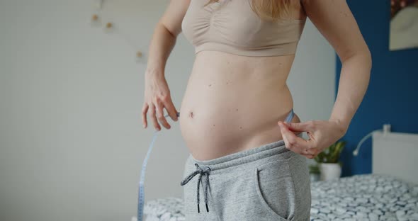Young Pregnant Woman Measures Abdominal Circumference with a Measuring Tape alt