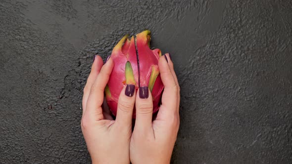 Closeup of Hands Breaking a Pitahaya Fruit in Half on a Black Background