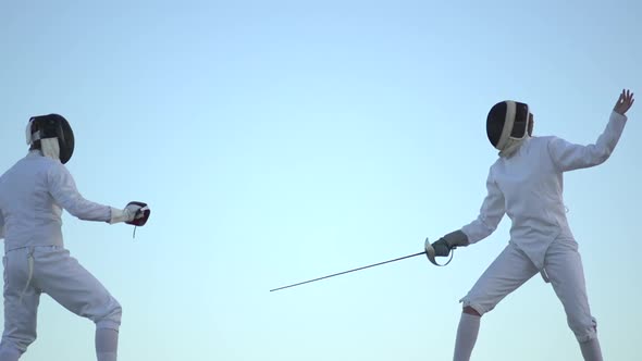 A man and woman fencing on the beach. alt