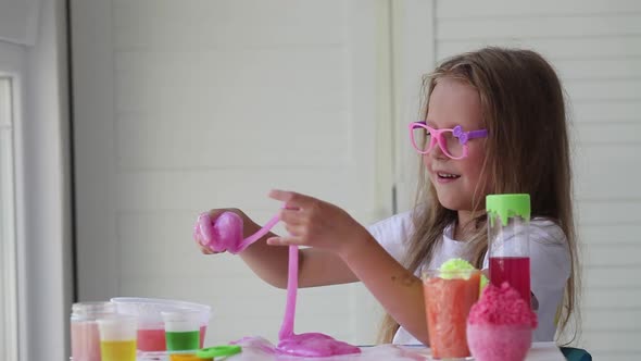 Little girl in glasses stretches a homemade pink slime and laughs