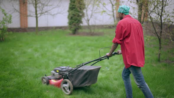 African American Young Man Walking with Lawnmower at Backyard alt