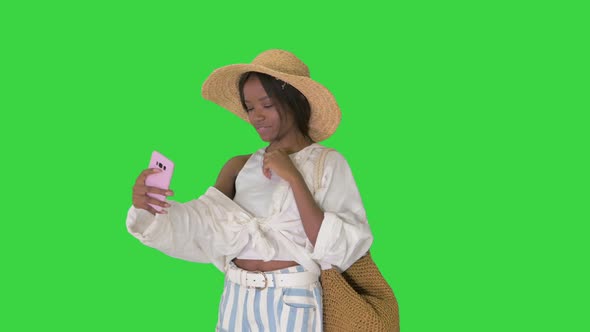 Smiling African American Woman Wearing Straw Hat and Taking Selfie on Smartphone on a Green Screen alt