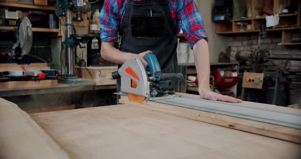 The Master Cuts a Wooden Board with a Circular Saw in the Woodworking Workshop of a Small Furniture alt
