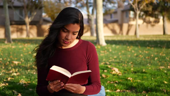 A young woman school girl studying and reading a book on a campus lawn or outdoor park SLOW MOTION. alt