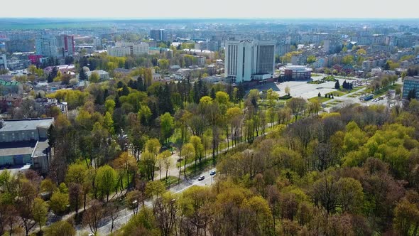 High altitude aerial view over the city at spring. Flight over the beautiful buildings and green tre alt