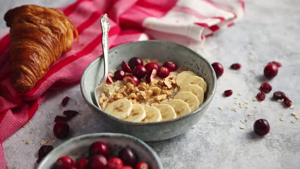 Ceramic Bowl of Oatmeal Porridge with Banana, Fresh Cranberries and Walnuts alt