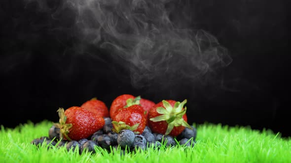 White smoke covering different fresh berries on grass surface alt