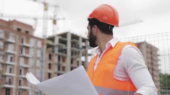 Construction Engineer Holding a Project in His Hand. He Checks a Drawing on the Construction Site alt