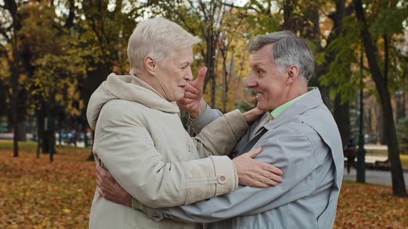 Joyful Middle Aged Elderly Couple Hugging Laughing Standing in Autumn Park Carefree Chatting Happy alt