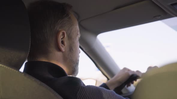 A Middleaged Handsome Caucasian Man Drives a Car on a Road  Rear Closeup From the Backseat