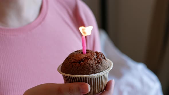 Woman holds a birthday cupcake with a candle in her hand and blows out the candle.